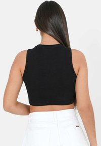 Top corto negro sin mangas con cuello redondo, diseño sin mangas y textura de canalé suave, combinado con pantalones blancos de tiro alto.