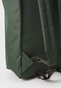 Sac à dos vert en tissu texturé, avec des sangles réglables et des coutures renforcées aux coins pour plus de solidité.