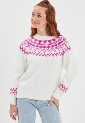 Maglione bianco lavorato a maglia con giogo a motivo rosa e dettagli zigzag sulle maniche. Texture morbida, collo tondo e orlo a coste. Abbinato a jeans blu.