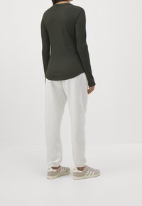 Mörkgrön ribbad långärmad topp med rundad nederkant, i kombination med vita sweatpants och grå sneakers med tre vita ränder.