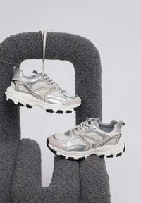 Srebrne i jasnoszare buty sportowe z teksturowanej siateczki i metalicznymi akcentami, z czarnymi gumowymi podeszwami i zapięciem na sznurówki.