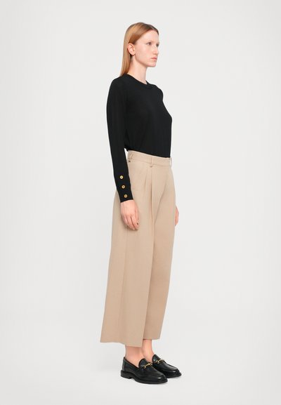 Sort langærmet bluse med knap detaljer ved manchetterne, parret med beige vide bukser. Sorte loafers fuldender outfittet.