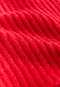 Tissu tricoté rouge avec une texture côtelée, comportant un fil doux et duveteux. Le matériau affiche une couleur uniforme et vibrante avec des côtes profondes.