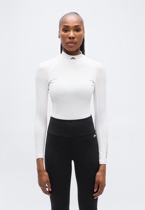 Hvit langermet topp med høy krage og svart logo, kombinert med svarte høytlivsleggings med en liten logo på siden.
