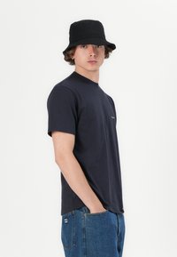Navy short-sleeve t-shirt with a round neck, made of soft material, paired with light blue denim jeans and a black bucket hat.