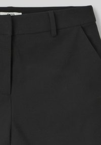 Pantalons noirs ajustés présentant une texture lisse, des plis à l'avant et des poches latérales. Fabriqués dans un tissu léger avec un design classique.