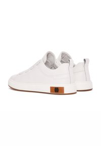 Zapatillas de cuero blanco con una textura suave, punta redondeada, costuras mínimas y un acento marrón en el talón que incluye un logotipo negro.