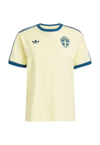 Svetložlté tričko s krátkym rukávom a modrými akcentmi, s okrúhlym výstrihom, modrými pruhmi na pleciach a švédskym erbom na hrudi.