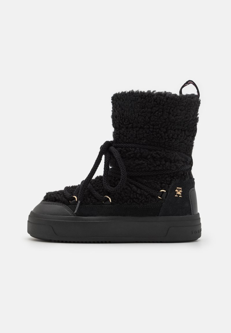 Zwarte enkelboot met een gestructureerde, pluizige bovenkant, suède accenten, vetersluiting en een contrasterende zwarte rubberen zool. Gouden hardwaredetail aanwezig.