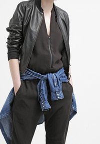 Czarna skórzana kurtka bombierka z ribbowymi mankietami, noszona na ciemnym body. Jasnoniebieska koszula dżinsowa przewiązana w talii, z detalami w postaci guzików.