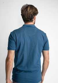 Camisa polo azul, de mangas cortas, con tejido texturizado y sutiles rayas, cuello y puños acanalados, silueta ajustada, vista trasera.