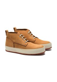 Bottines chukka en cuir tan avec un design montante, semelle en caoutchouc beige, cinq œillets de laçage et coutures contrastantes. Tige texturée et détail de l'étiquette.
