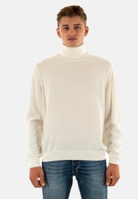 Maglione bianco a collo alto realizzato in morbido tessuto, con maniche lunghe e scollo a coste, abbinato a jeans blu.