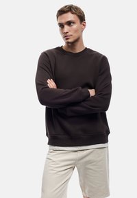 Donkerbruin sweatshirt met ronde hals en lange mouwen, textuurstof en geribbelde manchetten, gecombineerd met lichtbeige shorts.