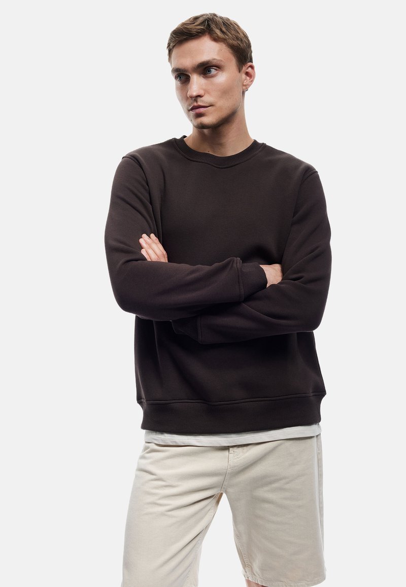Donkerbruin sweatshirt met ronde hals en lange mouwen, textuurstof en geribbelde manchetten, gecombineerd met lichtbeige shorts.