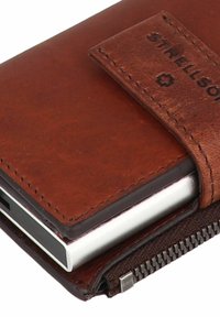 Portafoglio in pelle marrone con superficie teksturizzata, chiusura con zip e etichetta. Contiene una scheda argentata all'interno. Dettagli cuciti arricchiscono il design.