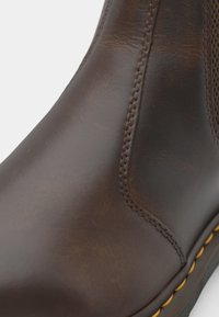 Braune Leder-Stiefelette mit elastischen Seiteneinsätzen, sichtbaren Nähten und einer kontrastierenden gelben Sohle. Glatte Textur mit glänzendem Finish.