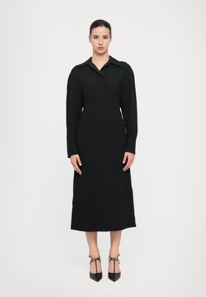 Black long-sleeve dress with a buttoned collar, straight silhouette, mid-calf length, made from a smooth fabric, paired with black pointed heels.