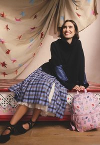 Fekete garbó csillogó ujjakkal, kék-fekete kockás szoknya, rózsaszín hátizsák állatmintákkal, fekete pántos cipők.