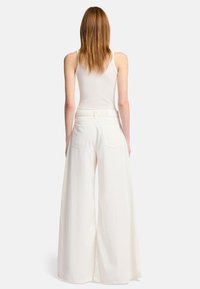 Witte wijde broek met hoge taille en grote achterzakken, gemaakt van lichte stof. Beschikt over een zachte textuur en strakke lijnen.