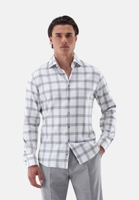 Camicia da uomo a maniche lunghe in tessuto bianco con motivo a quadri grigi; presenta una chiusura con bottoni sul davanti e un colletto classico.