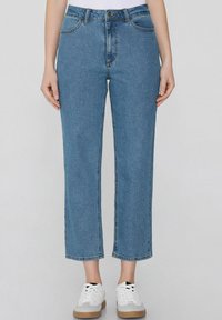 Vaqueros de mezclilla azul claro con corte recto, diseño de cinco bolsillos y detalles de costura visibles. Combinados con zapatillas blancas y una camiseta sencilla.