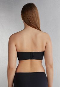 Zwarte strapless beha met een gladde textuur, voorzien van een veilige haak-en-oogsluiting aan de achterkant en een naadloos ontwerp.
