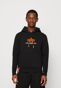Sudadera negra de mezcla de algodón con logo gráfico naranja. Cuenta con cordones, bolsillo canguro y etiqueta de marca roja en el dobladillo.