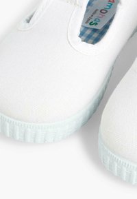 Scarpe slip-on bianche in tela con suola in gomma testurizzata, accenti blu chiaro a contrasto e una foderatura a scacchi visibile attraverso l'apertura della scarpa.