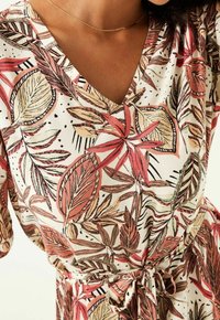 Sukienka w kwiaty z dekoltem w serek, z różowo-zielonym wzorem liści na kremowym tle, wiązana w talii, wykonana z lekkiego materiału.