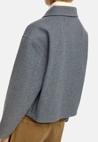 Szary żakiet z mieszanki wełny z wyraźnym kołnierzem, luźnym krojem i obniżonymi ramionami. Posiada prosty design z tyłu, idealny do noszenia na warstwy.