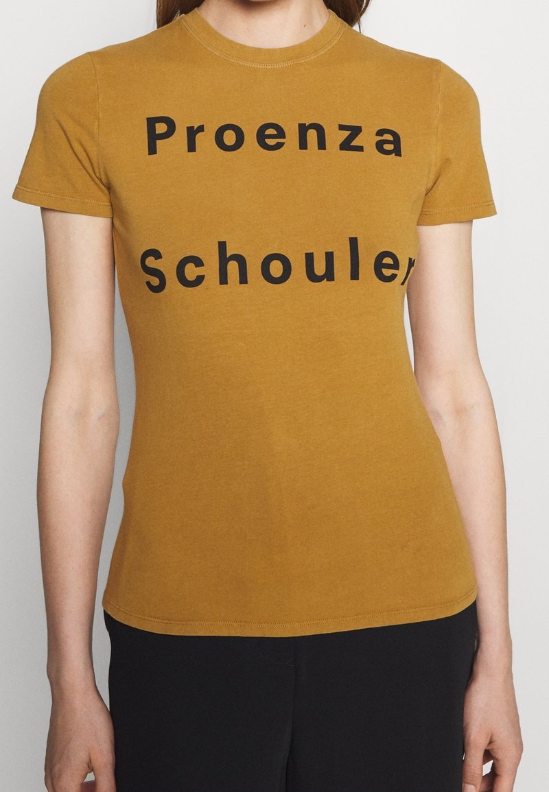 Senapsgul kortärmad t-shirt med svart text som säger "Proenza Schouler." Mjuk tyg med en figurnära design och rundad halsringning.