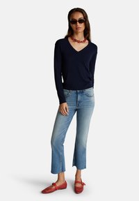 Námořnický svetr s V výstřihem, spárovaný se světle modrými zkrácenými džíny s bočními rozparky. Červené perforované baleríny a červený řetízkový náhrdelník dotvářejí vzhled.