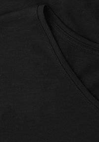 Gros plan sur un tissu noir montrant des coutures détaillées et l'encolure d'un vêtement, probablement un T-shirt ou un vêtement similaire.