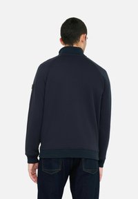 Marineblauer Pullover mit hohem Kragen, gerippten Bündchen und Saum. Glatte Textur und Raglanärmel. Minimale Markenkennzeichnung an der Schulter.