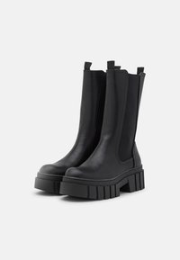 Mustan nilkkurit, joissa on paksu pohja, sileä nahkamateriaali, elastiset sivupaneelit ja vetonauhat helppoa päällepantavuutta varten.