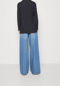 Námořnický blejzr s tenkými proužky a dlouhými rukávy, ve spojení s modrými džínami s širokými nohavicemi, které mají volný střih a detaily s třepení na lemu.