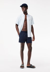 Himmelblaues Kurzarmhemd mit Knopfleiste, marineblaue Schwimmshorts, schwarze Badesandalen. Mit Logoakzenten, lockerer Passform und strandfertigem Stil.