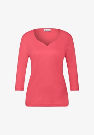 Koraalroze top met lange mouwen gemaakt van gladde stof, met een V-hals en een aansluitend silhouet. Eenvoudig ontwerp zonder patronen of extra versieringen.
