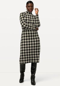 Abito midi in maglia con motivo a scacchi in nero e crema, dotato di colletto alto e maniche lunghe, abbinato a stivali neri sopra il ginocchio.