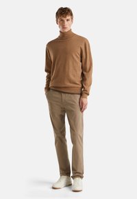 Brauner Rollkragenpullover aus weichem Material, kombiniert mit hellbeigen Chinos und weißen Sneakern. Schlichtes Design mit taillierter Silhouette.