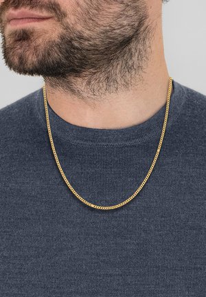 Collana di catena dorata con un design piatto e a maglie, indossata sopra un maglione blu navy a trama. La catena poggia sulla zona del colletto.