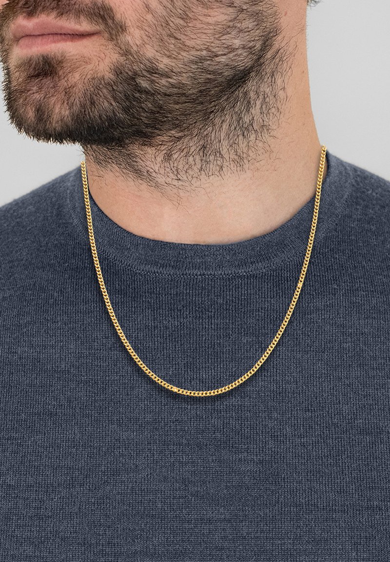 Guldkæde med flad, sammenkoblet design, båret over en struktureret mørkeblå sweater. Kæden ligger på kraveområdet.
