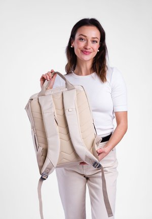 Beige backpack with quilted design, padded handles, and adjustable straps. Smooth texture, minimalistic shape, suitable for various uses.