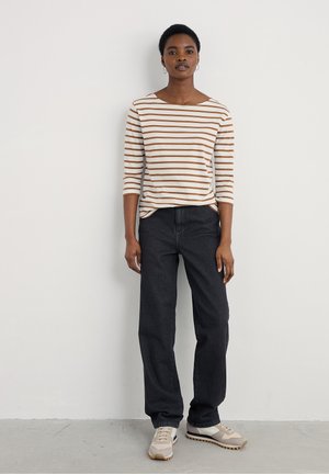 Striped long-sleeve top in cream and brown, paired with dark denim pants. Shoes are beige with grey and brown accents. Simple design, straight fit.
