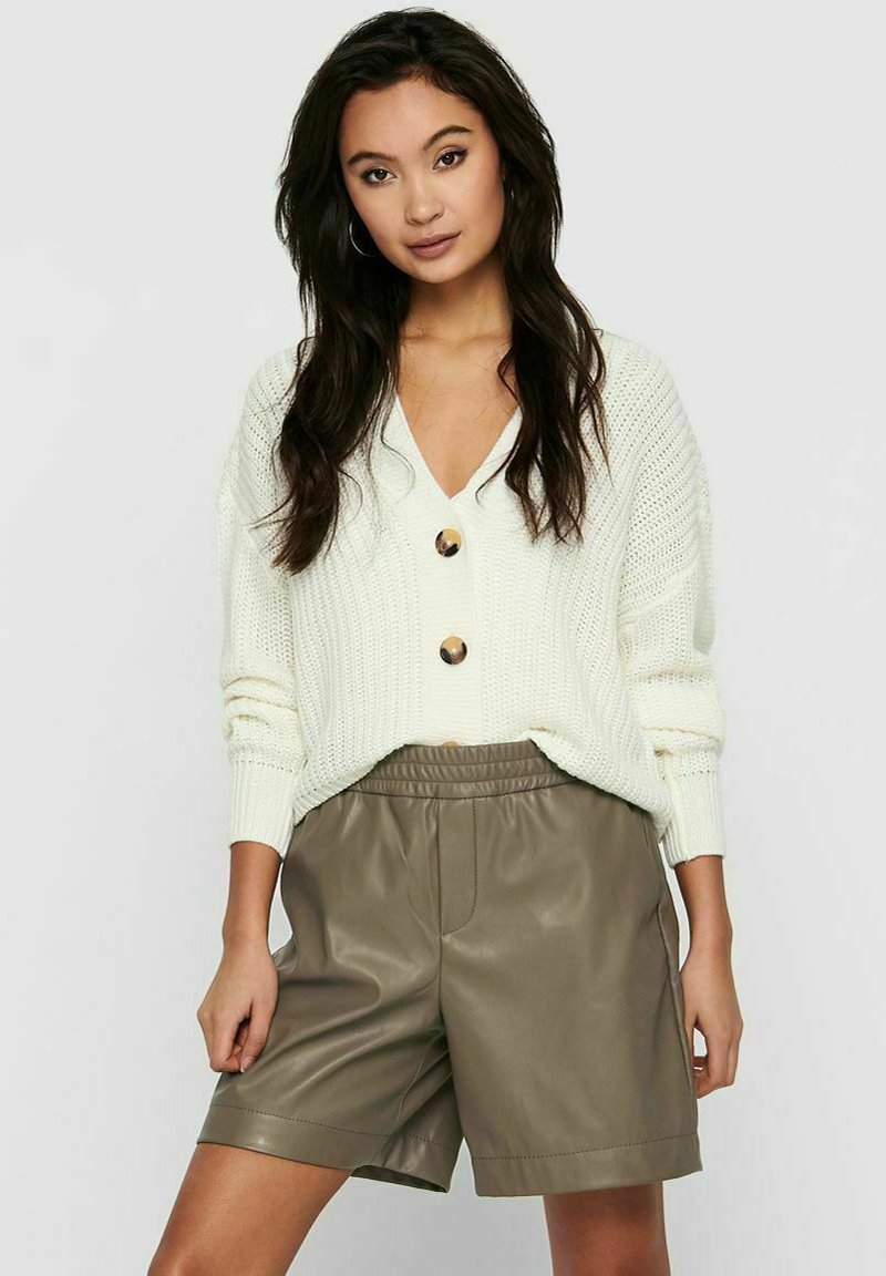 Lichtbeige gebreide cardigan met een v-hals en grote goudkleurige knopen, gecombineerd met olijfgroene leren shorts. Losse pasvorm en ribbelstructuur.