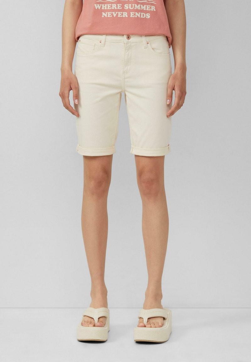 Beżowe bermudy dżinsowe z podwiniętymi mankietami, pięcioma kieszeniami i zapięciem na guzik, w połączeniu z jasnymi sandałami na platformie.