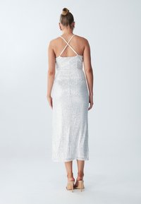 Silver sequin midi dress with a fitted silhouette and crisscross spaghetti straps, featuring a smooth texture and a straight hemline.