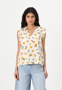Ärmlös topp i krämfärgad tyg med apelsin- och citrontryck, med V-ringning och avslappnad passform, matchad med ljusblå denimjeans.