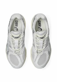 Scarpe sportive bianche con tomaia in rete e sovrapposizioni sintetiche, dotate di lacci, suola in gomma e branding in evidenza sulla linguetta e sui lati.